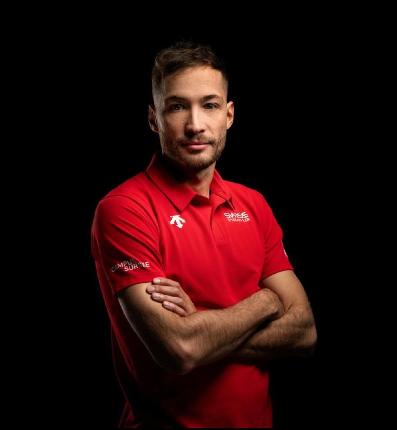 Sylvain Fridelance portant un polo de l'équipe de triathlon Suisse sur un fond noir.